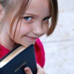 A little girl holds on to her father's Bible outside church.